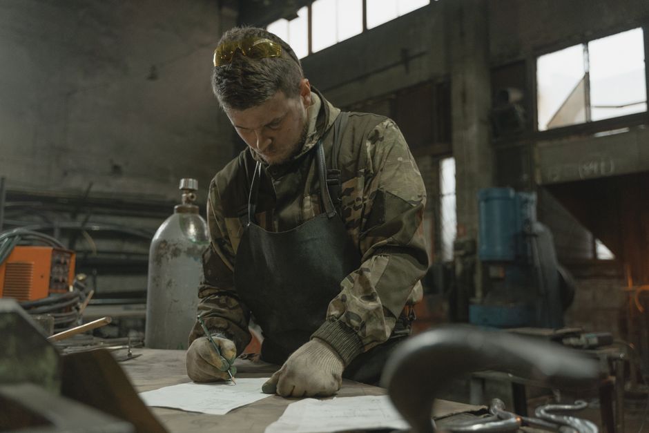 A man in a workshop writing notes while surrounded by metalwork equipment.